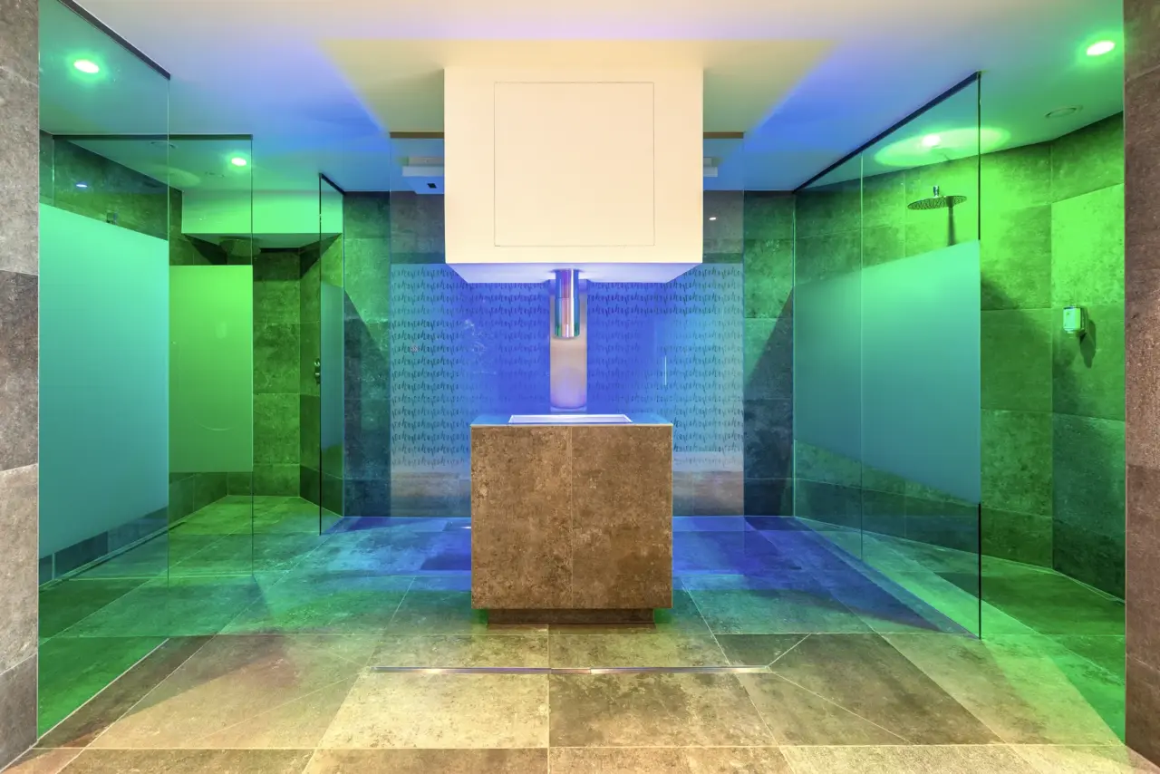 Modernes Badezimmer mit Glaswänden und farbigem Licht.
