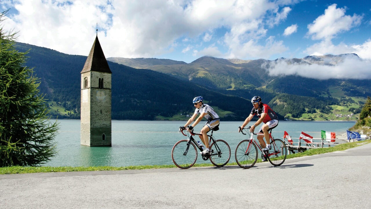 Radfahrer am Reschensee mit Kirchturm im Wasser
