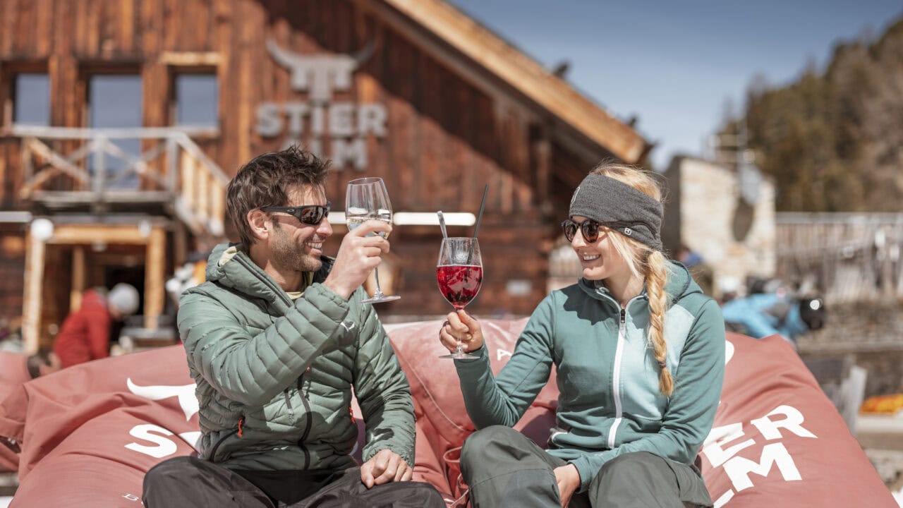 Zwei Personen stoßen vor alpiner Hütte an.