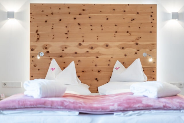 Gemütliches Doppelbett mit Holzrückwand und Bettwäsche.