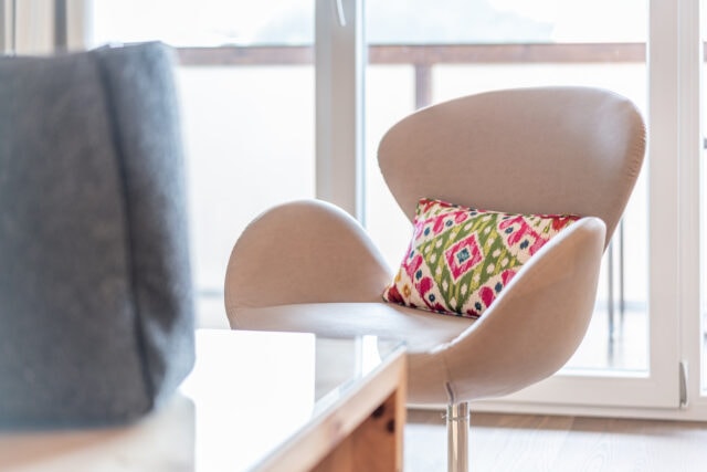 Eleganter Stuhl mit buntem Kissen vor Fenster.