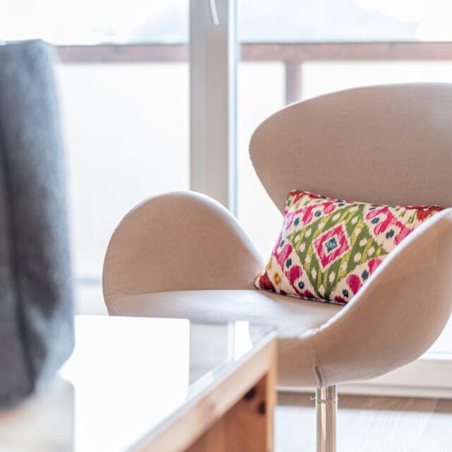 Eleganter Stuhl mit buntem Kissen vor Fenster.