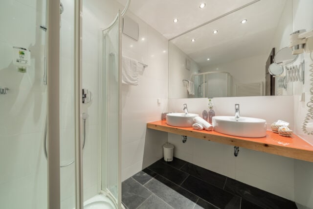 Sauberes Hotelbad im Naudererhof, moderne Ausstattung, Doppelwaschbecken, Wasserkocher, Wellness-Atmosphäre.