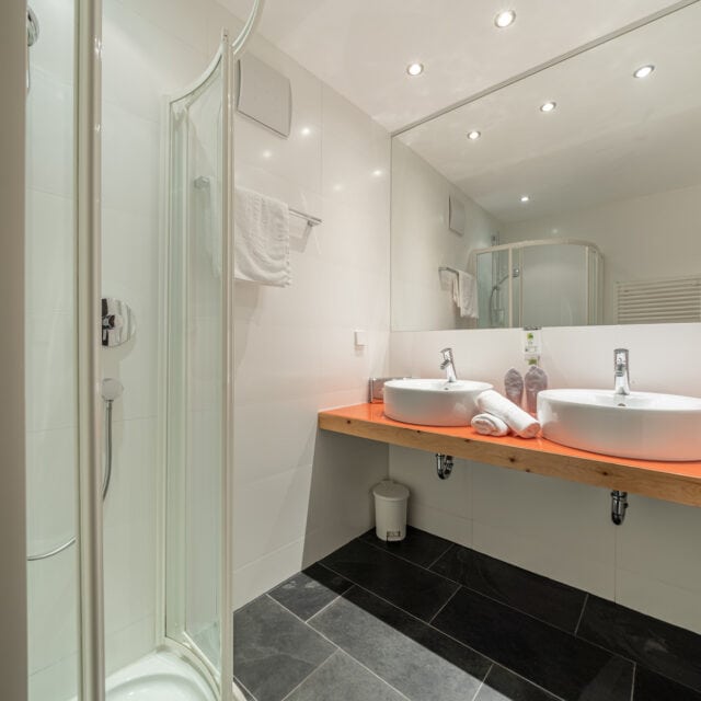 Sauberes Hotelbad im Naudererhof, moderne Ausstattung, Doppelwaschbecken, Wasserkocher, Wellness-Atmosphäre.