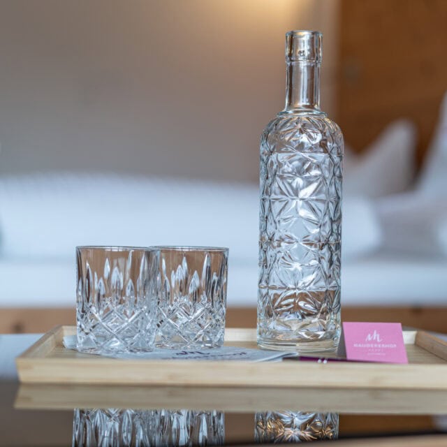 Glas und Karaffe aus Kristallglas auf Holzteller mit Naudererhof-Logo, hochwertiges Ambiente.