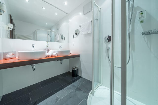 Sauberes Badezimmer mit Doppelwaschbecken und Dusche im Naudererhof, Tirol.