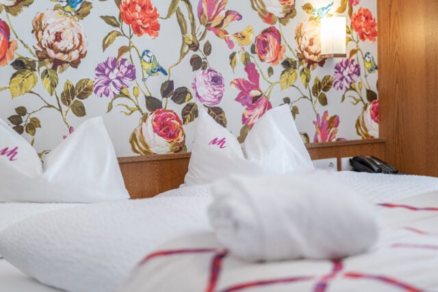 Blumenmuster-Wand hinter Hotelbett mit Kissen
