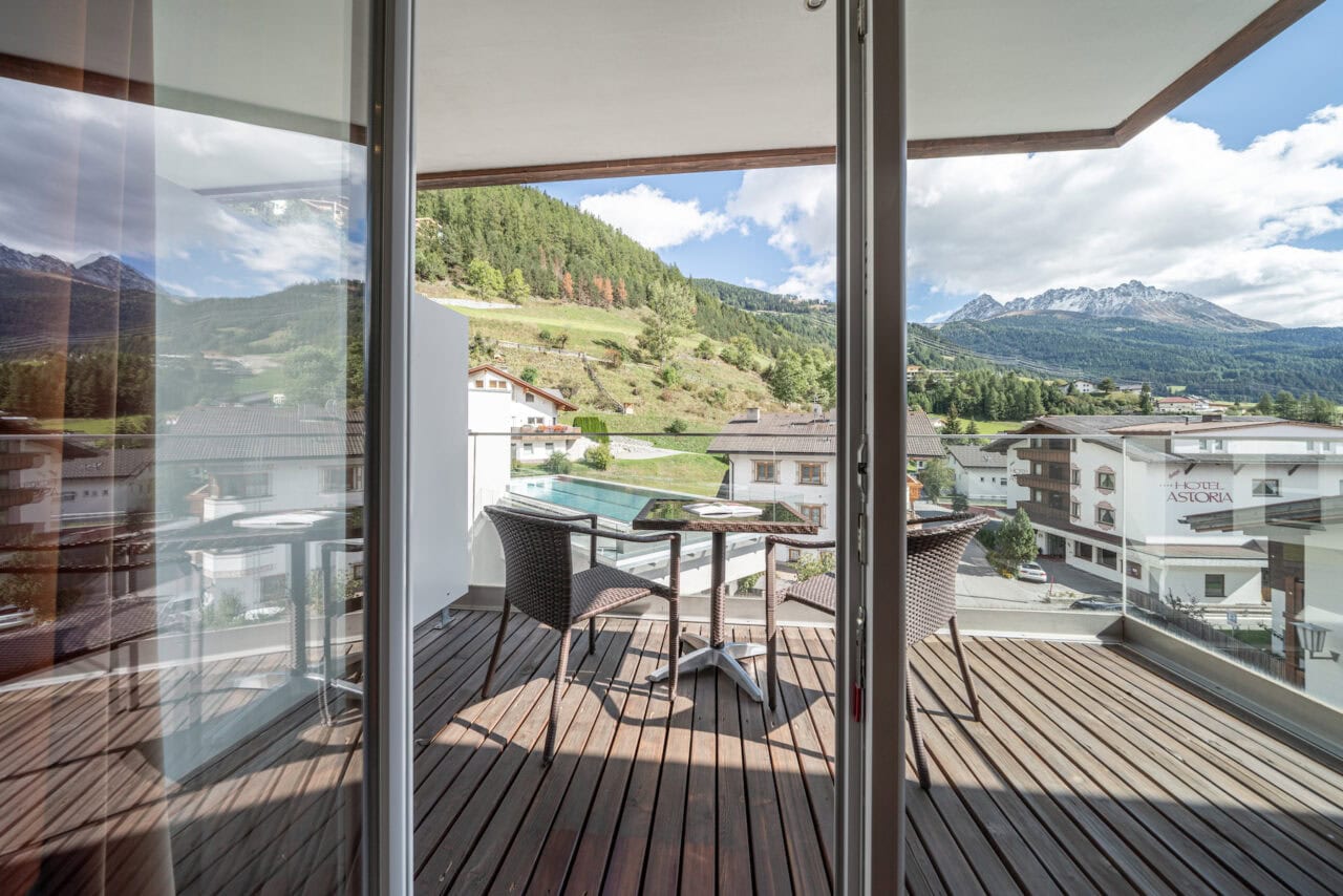 Balkon mit Sitzgelegenheit und Blick auf die in den Bergen umgebende Natur und das Dorf Nauders.