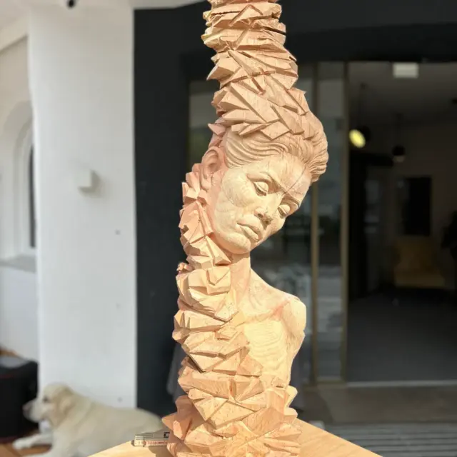 Holzskulptur auf Tisch, im Hintergrund liegt ein Hund.