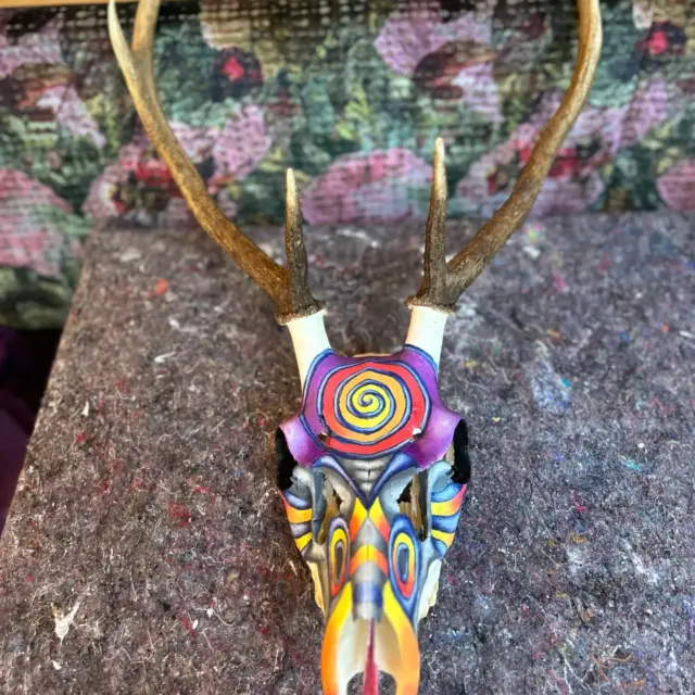 Bunt bemaltes Hirschgeweih vor floralem Hintergrund.