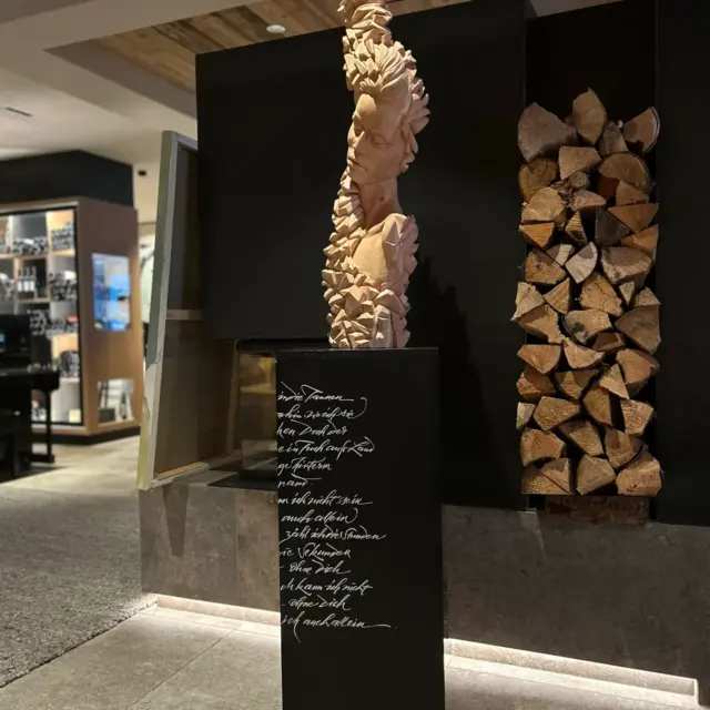 Holzskulptur auf schwarzem Sockel in modernem Raum