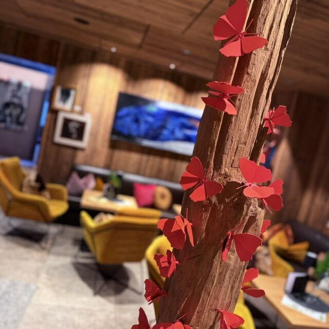 Rote Schmetterlings-Deko an Baumstamm, gemütliches Ambiente im Naudererhof, Inneneinrichtung, Holzdekor, Relax-Zone, rustikale Atmosphäre.