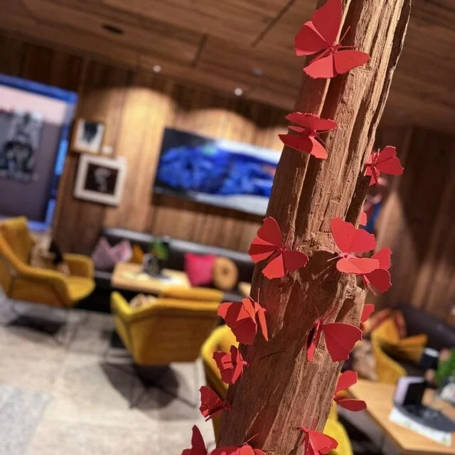 Rote Schmetterlings-Deko an Baumstamm, gemütliches Ambiente im Naudererhof, Inneneinrichtung, Holzdekor, Relax-Zone, rustikale Atmosphäre.