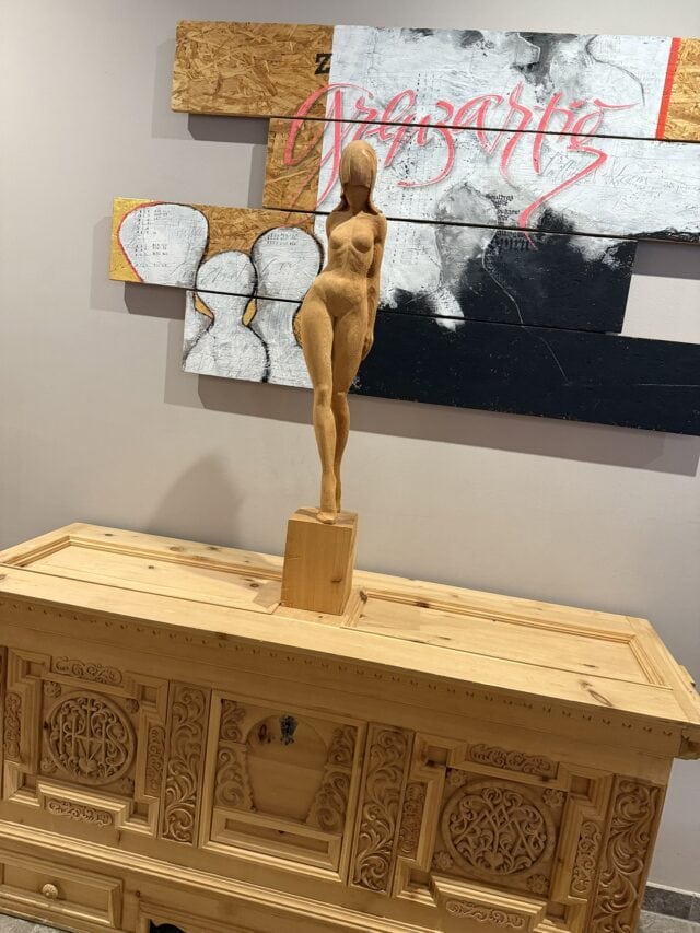Holzfigur auf kunstvoller Kommode vor Wandkunst.
