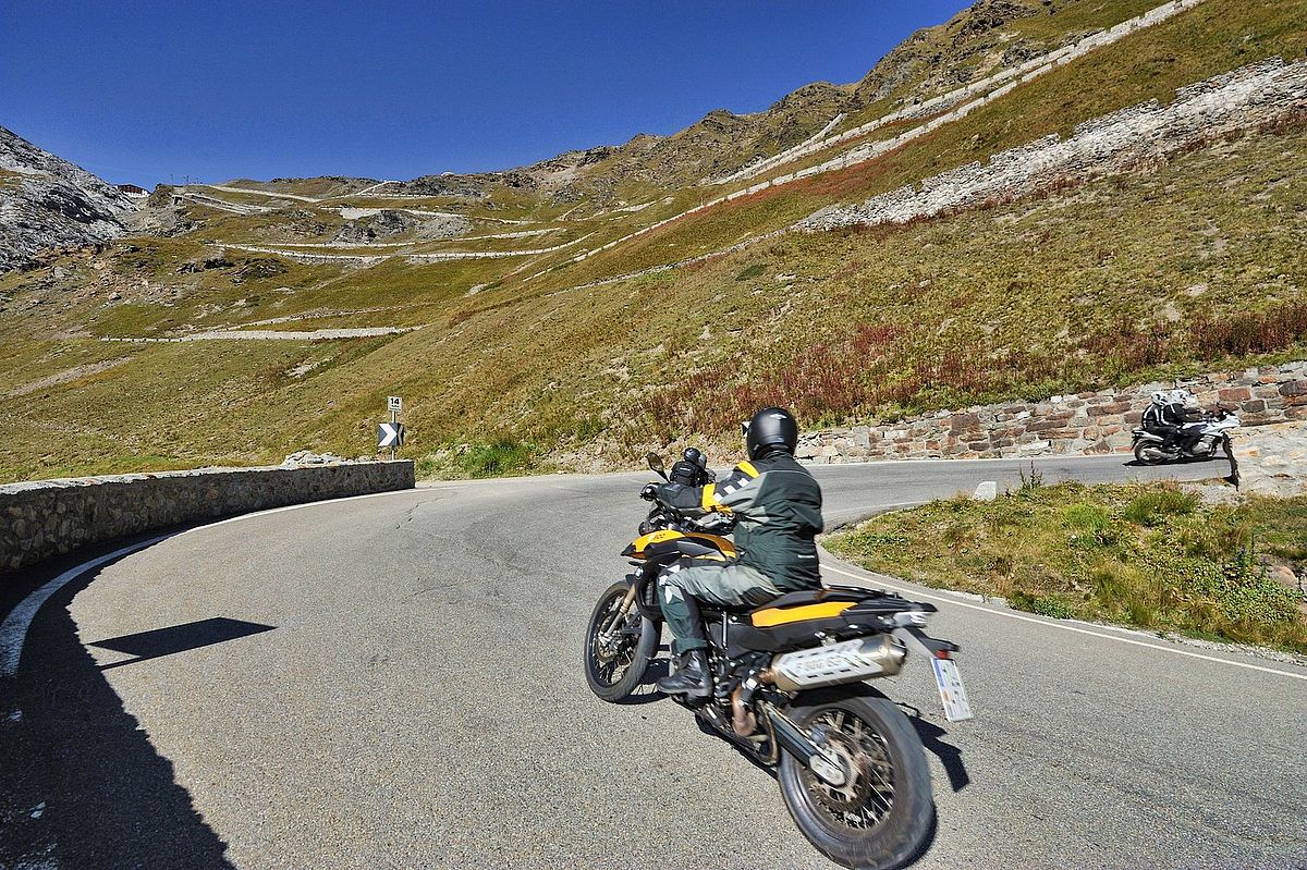 Motorradfahrer auf einer kurvigen Bergstraße bei Sonnenschein.