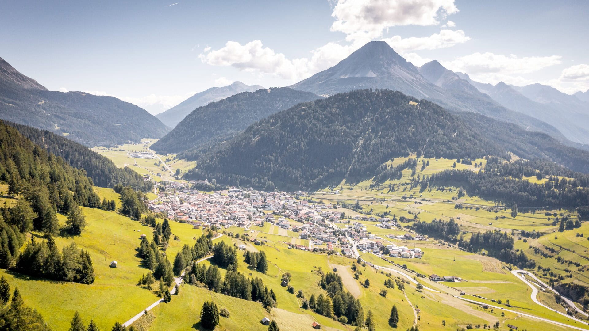 Berglandschaft mit Dorf im Tal bei Sonnenschein.