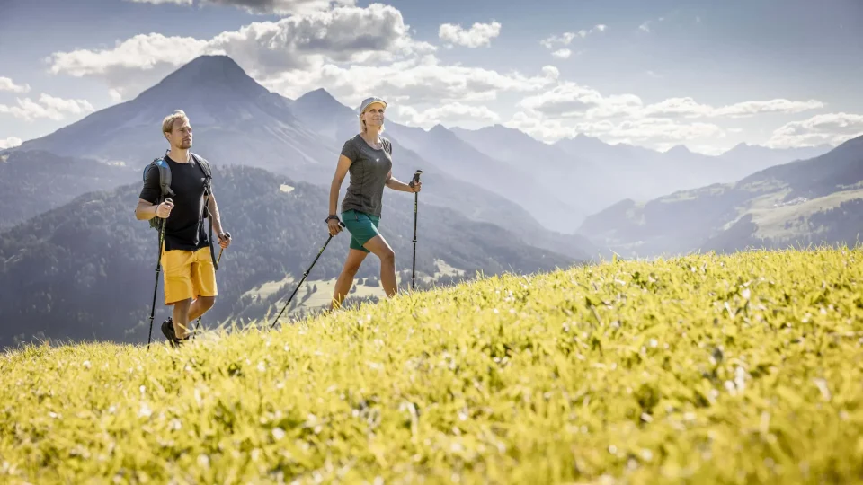 Zwei Wanderer in alpiner Landschaft bei Sonnenschein.