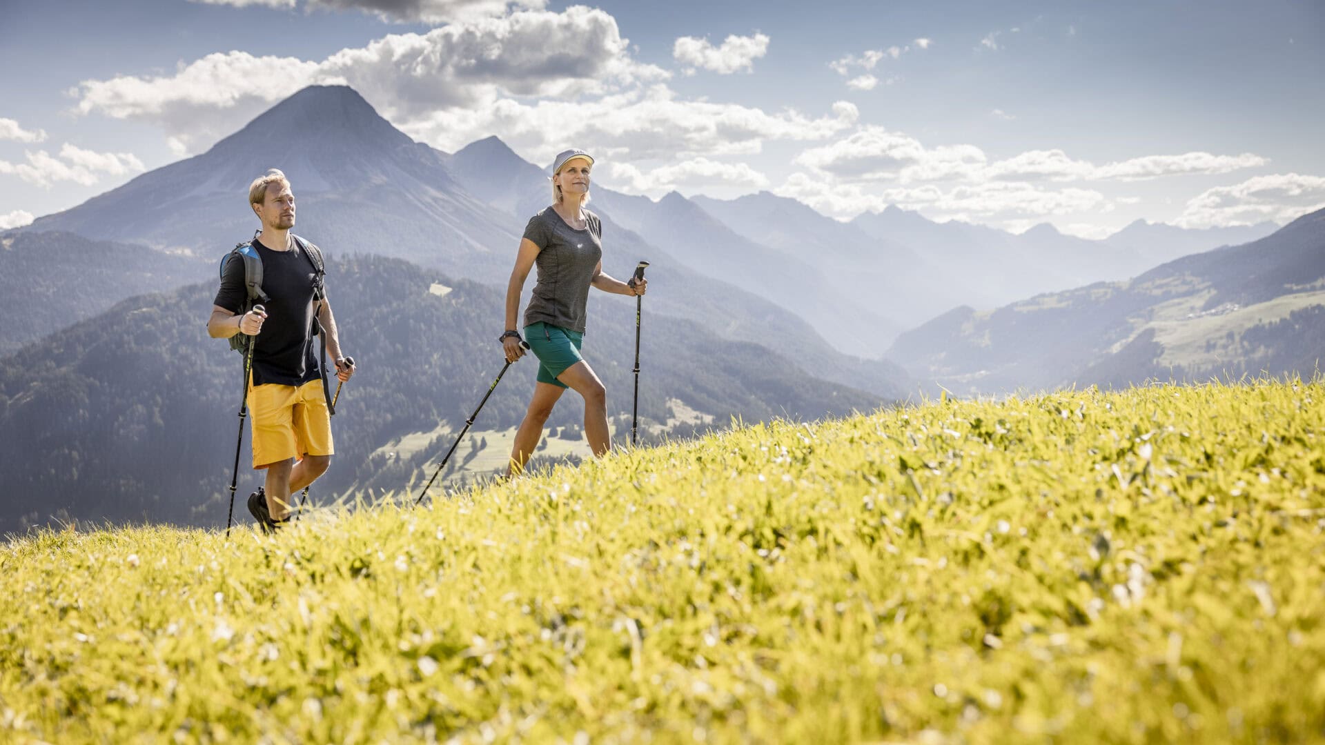 Zwei Wanderer in alpiner Landschaft bei Sonnenschein.