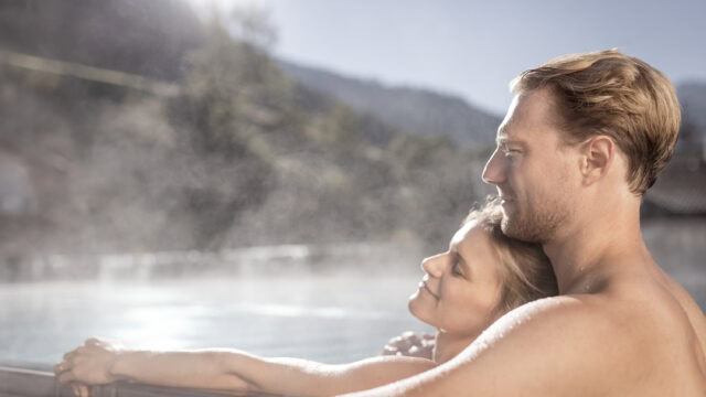 Paar entspannt im Thermalbad mit Bergen im Hintergrund