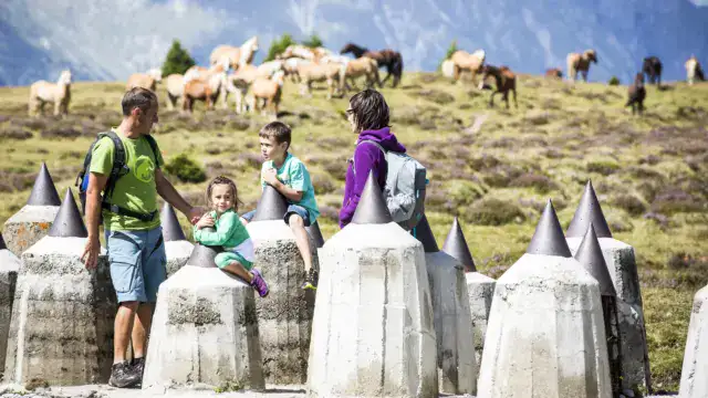 Familie wandert in den Bergen mit Pferden im Hintergrund.