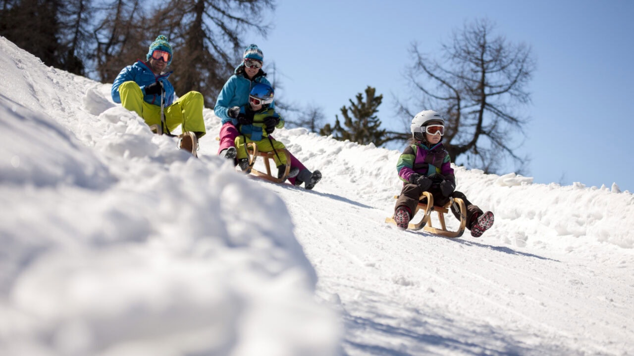 Familie beim Rodeln im Schnee unter blauem Himmel.