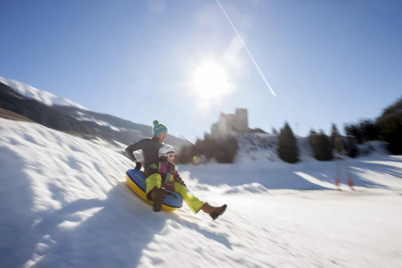Zwei Personen beim Schneerodeln im Sonnenschein.