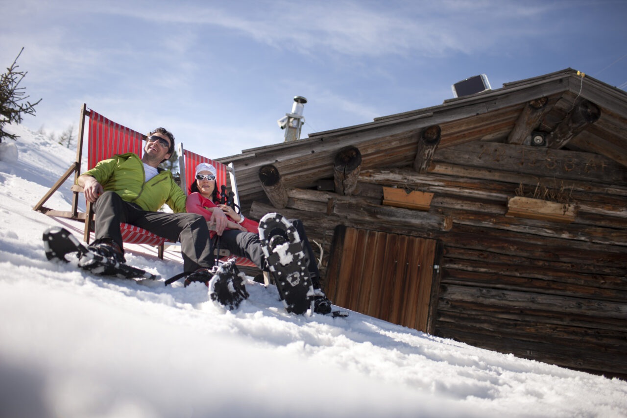 Menschen entspannen im Schnee vor Hütte