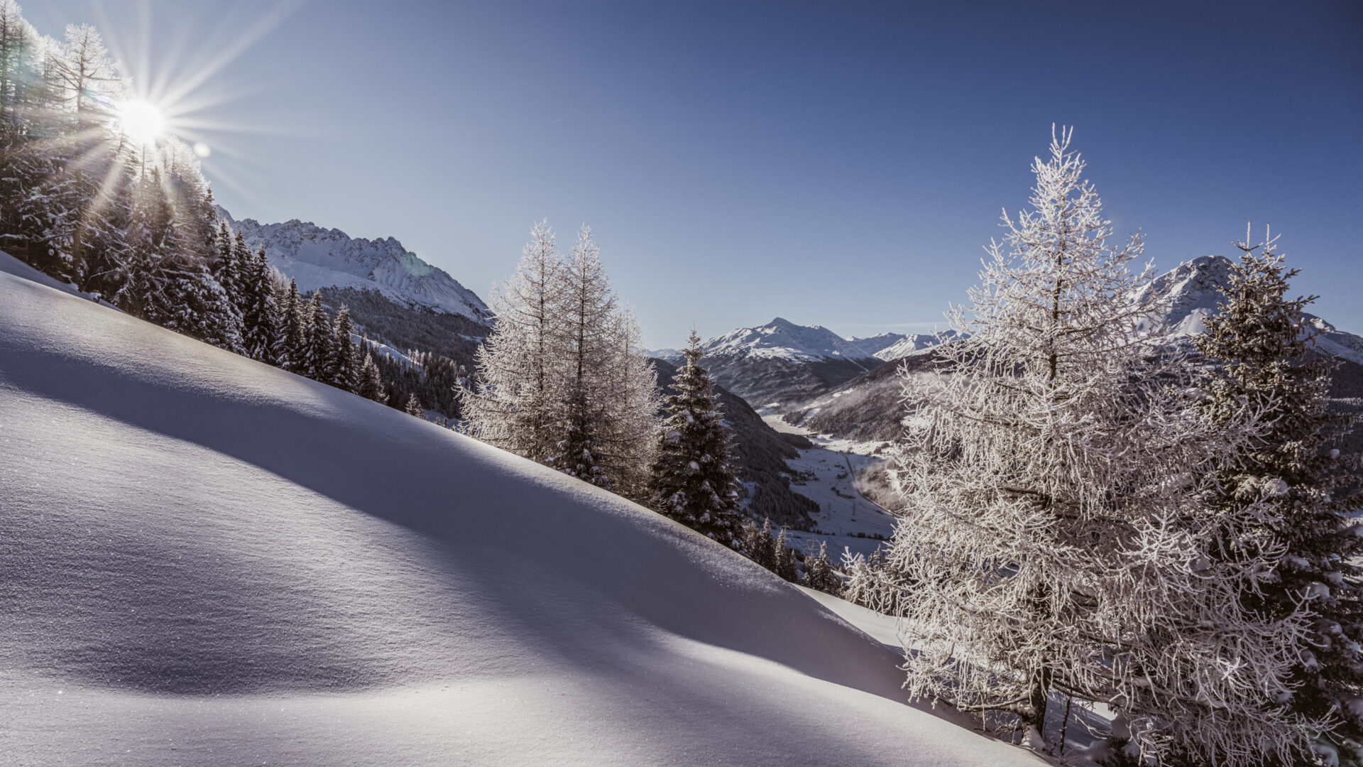 Verschneite Berglandschaft bei Sonnenschein und blauem Himmel.