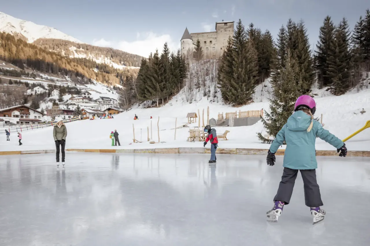 Kinder eislaufen im Schnee vor einer Burg.