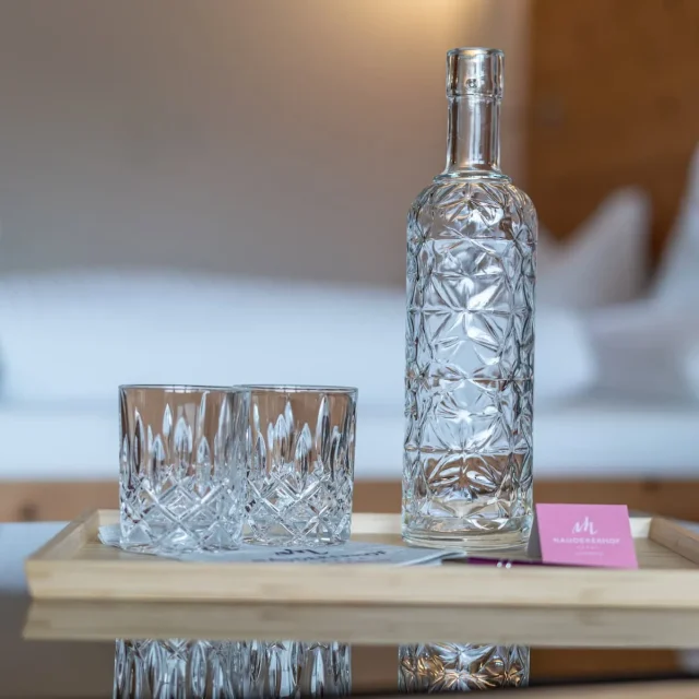 Glas und Karaffe aus Kristallglas auf Holzteller mit Naudererhof-Logo, hochwertiges Ambiente.