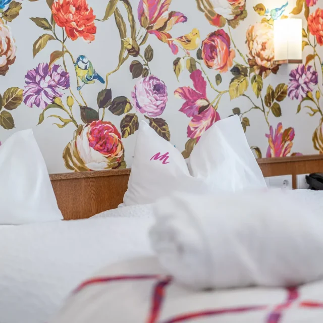 Blumenmuster-Wand hinter Hotelbett mit Kissen