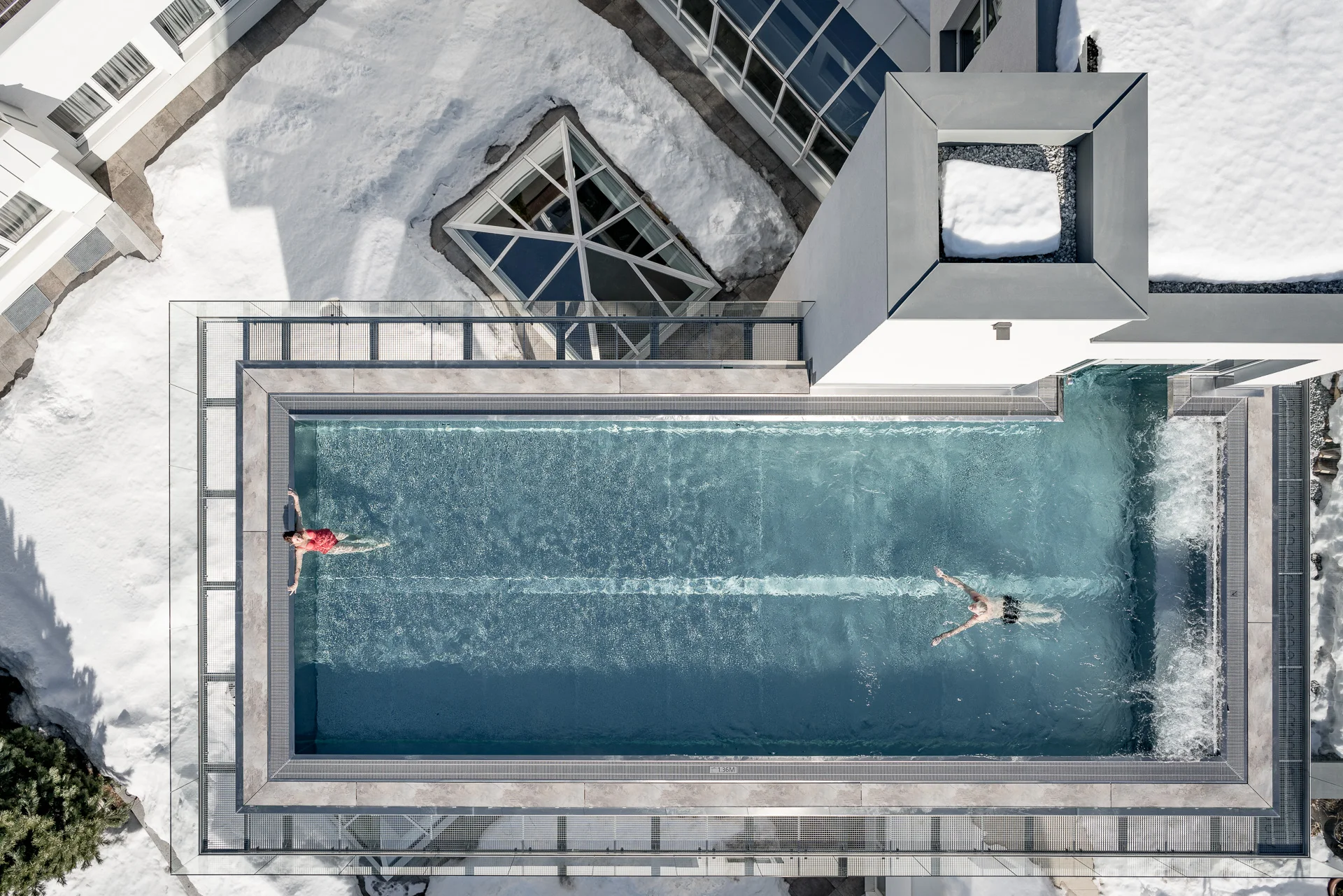 Luftaufnahme eines Außenpools im Schnee mit zwei Schwimmern.